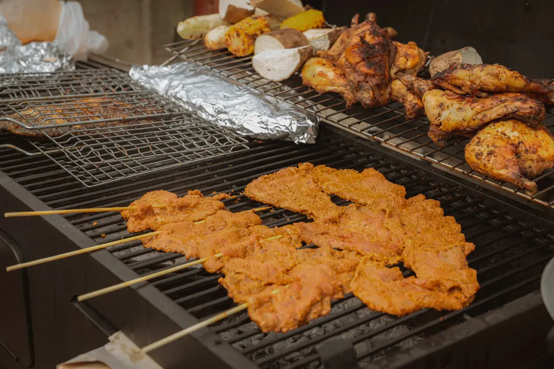 Outdoor grill with suya skewers, chicken, corn, and yam