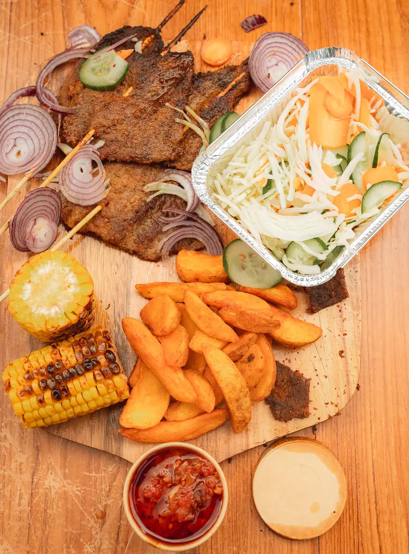Suya platter with potato wedges, salad, roasted corn, and sauce