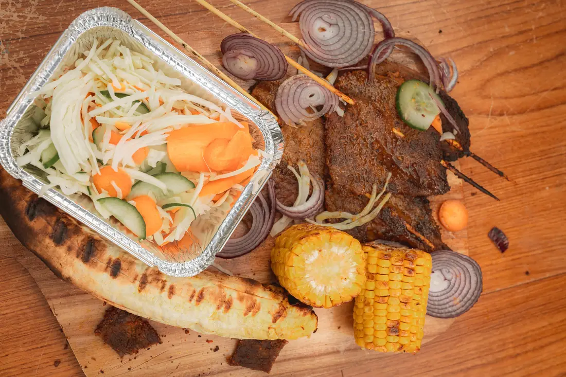 Suya served with plantain, salad, and roasted corn